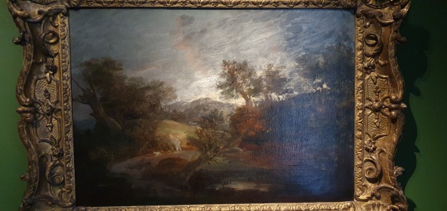 "Landscape scene with big grey and red lit up sky, trees leaning to the left, hills in the disatnce."