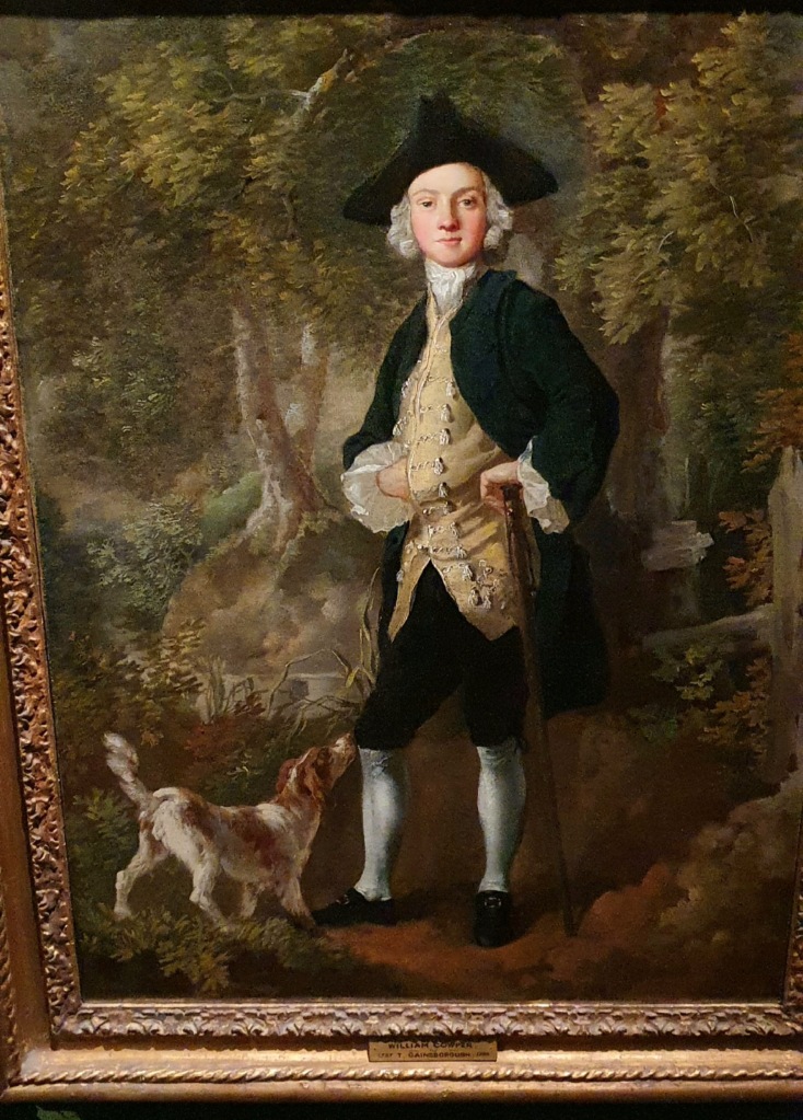 "Georgian man with triangular hat, black long coat, gold waitscoat and dog at his fee, surrounded by trees."