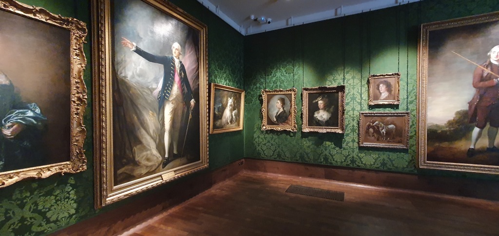 "Green silk woven gallery walls and on these a various set of large and smaller paintings by Gainsbrorough. Quite dark and wooden floor."
